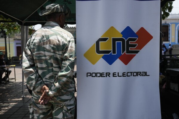 FILE - A Bolivarian Militia member stands on guard next to a banner of the National Electoral Council (CNE) where people can register to vote in the presidential election in Caracas, Venezuela, April 16, 2024. On May 28, 2024, Venezuela’s electoral authorities revoked an invitation for a European Union mission to observe the country's July 28 presidential election. (AP Photo/Ariana Cubillos, File)