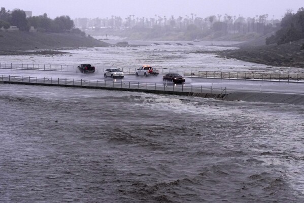 Vehicles cross over a flood control basin that has almost reached the street, Sunday, Aug. 20, 2023, in Palm Desert, Calif. Forecasters said Tropical Storm Hilary was the first tropical storm to hit Southern California in 84 years, bringing the potential for flash floods, mudslides, isolated tornadoes, high winds and power outages. (AP Photo/Mark J. Terrill)