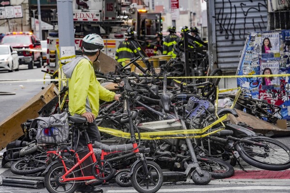 FILE - A biker stops to look at a pile of e-bikes in the aftermath of a fire in Chinatown, which authorities say started at an e-bike shop and spread to upper-floor apartments, Tuesday June 20, 2023, in New York. New York City is receiving $25 million in emergency funding from the U.S. Department of Transportation to establish scores of new e-bike charging stations across the city. Mayor Eric Adams announced the funding Sunday, June 25. (AP Photo/Bebeto Matthews, File)