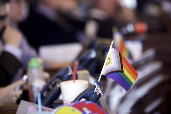 FILE - A flag supporting LGBTQ+ rights decorates a desk on the Democratic side of the Kansas House of Representatives during a debate, March 28, 2023, at the Statehouse in Topeka, Kan. Children are heading back to classes and fall sports practices, and four more states are expecting their K-12 schools to keep transgender girls off their girls sports teams. Kansas, North Dakota and Wyoming had new laws restricting transgender athletes in place before classes resumed, and a Missouri law takes effect at the end of this month. (AP Photo/John Hanna, File)