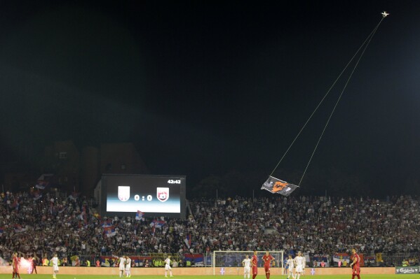 FILE- A drone with an Albanian flag flies over Partizan stadium during the Euro 2016 Group I qualifying match between Serbia and Albania in Belgrade, Serbia on Oct. 14, 2014. A tournament co-hosting bid by Albania and Serbia is an unlikely project in European soccer and politics. The Balkan neighbors’ soccer federations have surprisingly teamed up to persuade UEFA to award them the men’s Under-21 European Championship. (AP Photo/Darko Vojinovic, Files)