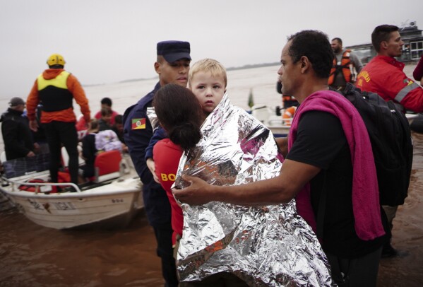 أحد أفراد الدفاع المدني يحمل طفلاً تم إنقاذه من منطقة غمرتها الأمطار الغزيرة في بورتو أليغري، ولاية ريو غراندي دو سول، البرازيل، السبت 4 مايو 2024. (AP Photo / Carlos Macedo)