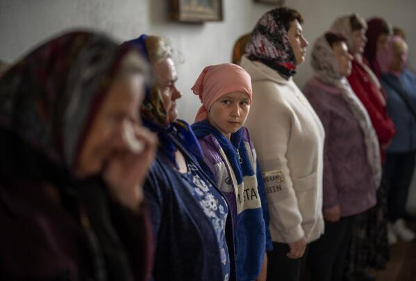 A girl looks towards a woman crying during a religious service to commemorate the fallen during the Russian occupation in Zdvyzhivka, Ukraine, on the outskirts of Kyiv, on Saturday, April 30, 2022. (AP Photo/Emilio Morenatti)