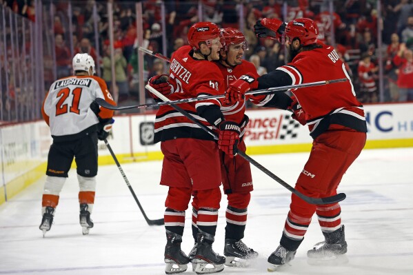 Carolina Hurricanes' Seth Jarvis, center, celebrates after his winning overtime goal with teammates Brent Burns, right, and Jake Guentzel (59) as Philadelphia Flyers' Scott Laughton (21) skates past at an NHL hockey game in Raleigh, N.C., Thursday, March 21, 2024. (AP Photo/Karl B DeBlaker)