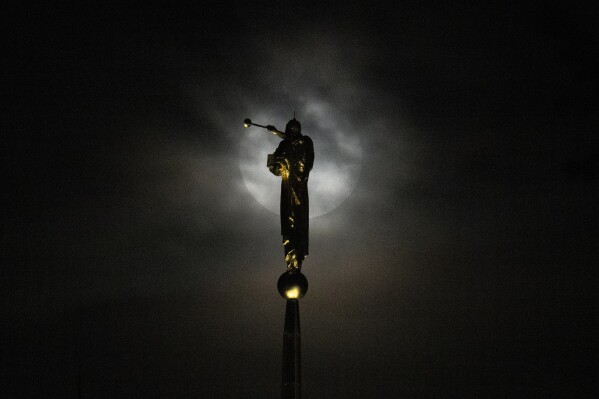 The supermoon, blue moon, rises behind a thick layer of clouds near a statue of the angel Moroni perched atop The Church of Jesus Christ of Latter-day Saints, Wednesday, Aug. 30, 2023, in Kensington, Md. (AP Photo/Julio Cortez)