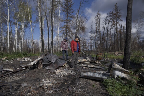 Happy Cardinal, right, looks at what remains of his cabin, destroyed by wildfires, near Fort Chipewyan, Canada, on Sunday, Sep. 3, 2023. Wildfires are bringing fresh scrutiny to Canada's fossil fuel dominance, its environmentally friendly image and the viability of becoming carbon neutral by 2050. (Ǻ Photo/Victor R. Caivano)