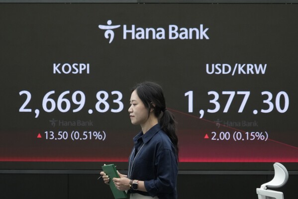 A currency trader passes by the screen showing the Korea Composite Stock Price Index (KOSPI), left, and the foreign exchange rate between U.S. dollar and South Korean won at the foreign exchange dealing room of the KEB Hana Bank headquarters in Seoul, South Korea, Monday, April 29, 2024. (AP Photo/Ahn Young-joon)