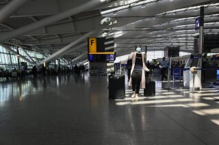 FILE - In this Tuesday, March 24, 2020 file photo, a woman wears a mask as she walks through a quieter than usual Heathrow Airport Terminal 5, in London. Air traffic is down 92% this year as travelers worry about catching COVID-19 and government travel bans and quarantine rules make planning difficult. One thing airlines believe could help is to have rapid virus tests of all passengers before departure. (AP Photo/Kirsty Wigglesworth, File)