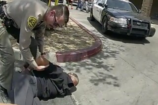 In this image taken from police body camera provided by Los Angeles Sheriff's office on June 24, 2023, a Sheriff's deputies arrested a couple in a grocery store parking lot in Lancaster, Calif. The Los Angeles County sheriff has opened an investigation into two deputies' actions after a bystander's cellphone footage showed one of them tackling a woman while she filmed her husband being handcuffed in what the scandal-ridden department described as disturbing. (Los Angeles County Sheriff's Office via AP)