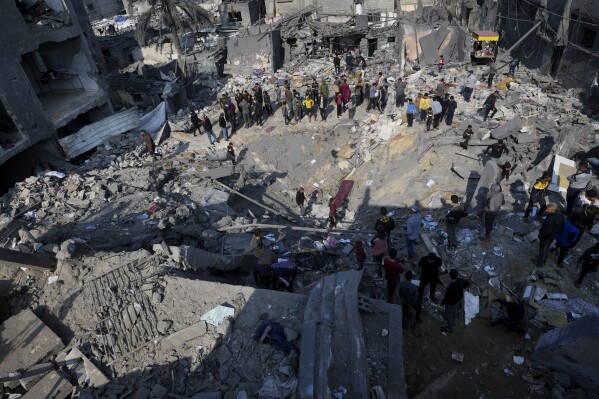 FILE - Palestinians look at the destruction of the al-Ghatshan family building after an Israeli attack in the Nusrat refugee camp in the central Gaza Strip on December 18, 2023.  The Israeli military campaign against Hamas has now come to a close, after an 11-week war in Gaza, one of the deadliest and most destructive in history.  The Palestinian death toll is approaching 20,000 and satellite data shows a third of the structures in the small area have been destroyed.  (AP Photo/Adele Hana, File)