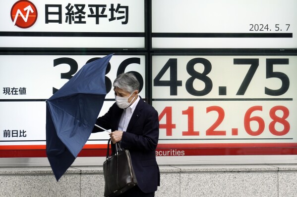 A person walks in the rain near an electronic stock board showing Japan's Nikkei 225 index at a securities firm Tuesday, May 7, 2024, in Tokyo. (AP Photo/Eugene Hoshiko)