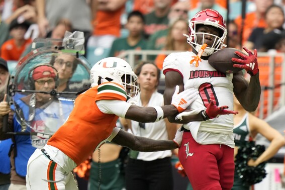 Louisville wide receiver Chris Bell (0) makes a catch against Miami defensive back Damari Brown (6) during the first half of an NCAA college football game, Saturday, Nov. 18, 2023, in Miami Gardens, Fla. (AP Photo/Wilfredo Lee)