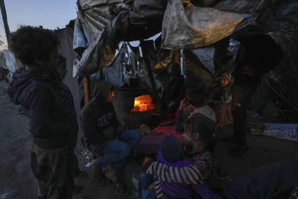 Displaced Palestinians sit next to a makeshift oven as breads are baked in a tent set up on an area in Deir al-Balah, Gaza Strip Thursday, Dec. 5, 2024. (AP Photo/Abdel Kareem Hana)