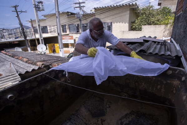 Augusto Cesar, a city worker who combats endemic diseases, places netting over a water tank where mosquitoes can breed, to help eradicate the Aedes aegypti mosquito which can spread dengue, in the Morro da Penha favela of Niteroi, Brazil, Friday, March 1, 2024. (AP Photo/Bruna Prado)
