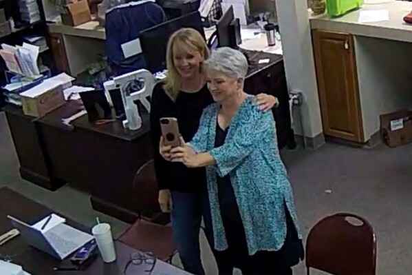 FILE - In this Jan. 7, 2021, image taken from Coffee County, Ga., security video, Cathy Latham, right, appears to take a selfie with a member of a computer forensics team inside the local elections office. Lawyers for three Georgia Republicans, including Latham, who falsely claimed that Donald Trump won the state and they were “duly elected and qualified” electors, are set to argue that their criminal charges should be moved from state to federal court(Coffee County, Georgia via AP)