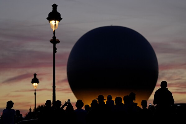 People wait for the balloon carrying the Olympic cauldron to rise above Tuileries Garden during the 2024 Summer Olympics, Tuesday, Aug. 6, 2024, in Paris, France. (AP Photo/Charlie Riedel)