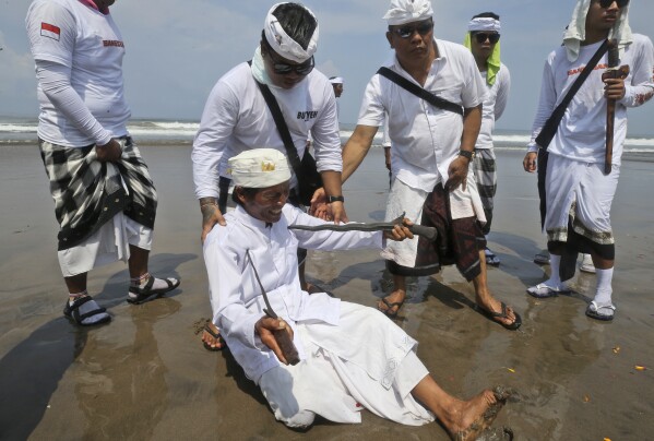 A Devout Balinese Hindu enters into a trance and pierces himself with metal swords while chanting prayers, on Melasti at Petitenget beach in Bali, Indonesia on Friday, March 8, 2024. Melasti is part of the six-day long Balinese Hindu New Year, where devout perform rituals as an act of symbolic cleansing. (AP Photo/Firdia Lisnawati)