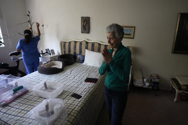 Catia Lattouf thanks a young man for bringing her a baby hummingbird he rescued, as her collaborator Cecilia Santos feeds a charm of hummingbirds in the background, in her apartment that she has turned into a makeshift clinic for the tiny birds, in Mexico City, Monday, Aug. 7, 2023. Lattouf says she never turns away a bird. (AP Photo/Fernando Llano)