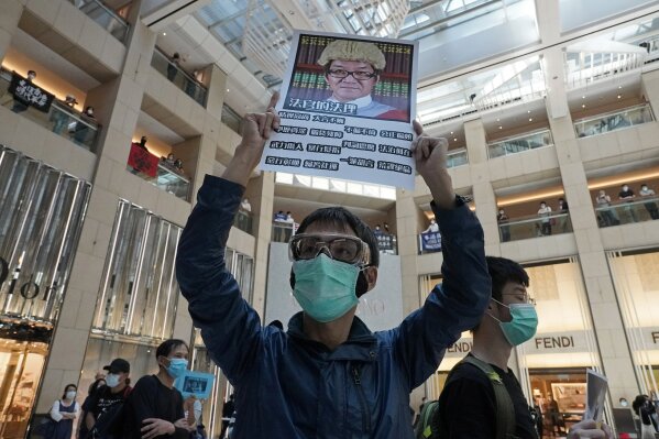 A protestor wearing a face mask raises a placard condemning a judge who likened protesters to terrorists and has since been barred from handling cases related to the demonstrations during a protest at a shopping mall Hong Kong, Wednesday, April 29, 2020. Demonstrators gathered in a luxury mall chanting pro-democracy slogans, the latest in a string of protests over the past week. (AP Photo/Vincent Yu)