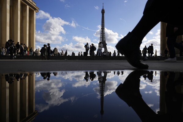 FILE - The Eiffel Tower is reflected in a puddle as people walk past at the Trocadero square, in Paris, France, Tuesday, Oct. 24, 2023. The word "Quoicoubeh!," became super popular this year with French teenagers who used it to annoy their elders, though it doesn't have a real meaning. It's simple: A teen says something inaudible, hoping that parents or teachers will answer "Quoi?" or "What?" The response : "Quoicoubeh!"(AP Photo/Pavel Golovkin, File)