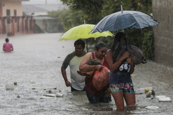 Residentes caminan por una carretera inundada con algunas pertenencias en Progreso Yoro, Honduras, el miércoles 4 de noviembre de 2020. (AP Foto/Delmer Martinez)
