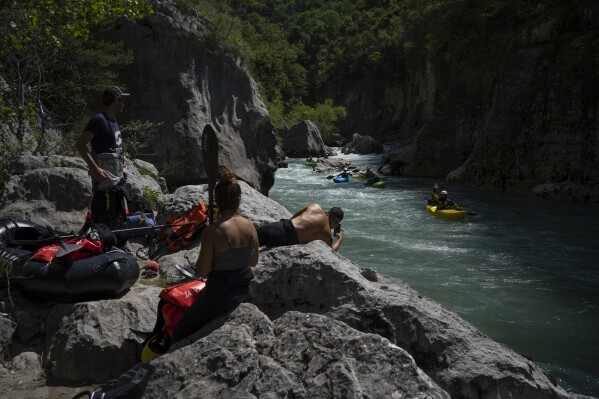 A kayaker waves to tourists preparing to packraft along the Verdon Gorge in southern France, Monday, June 19, 2023. Human-caused climate change is lengthening droughts in southern France, meaning the reservoirs are increasingly drained to lower levels to maintain the power generation and water supply needed for nearby towns and cities. It's concerning those in the tourism industry, who are working out how to keep their lakeside businesses afloat. (AP Photo/Daniel Cole)