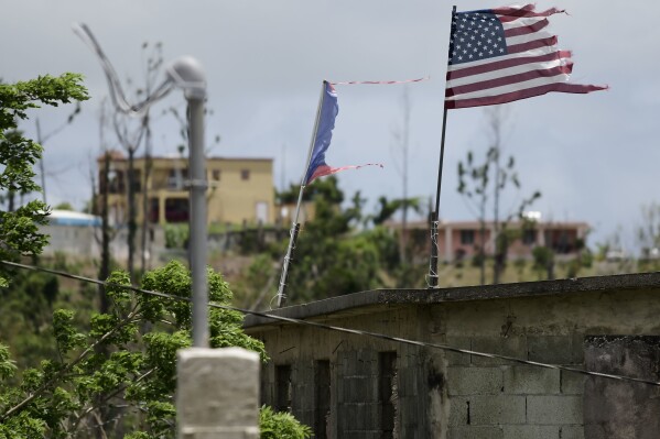 FILE - Deteriorated U.S. and Puerto Rico flags fly on a roof eight months after the passing of Hurricane Maria in the Barrio Jacana Piedra Blanca area of Yabucoa, a town where many continue without power in Puerto Rico, May 16, 2018. A federal judge on Tuesday, Nov. 14, 2023, tentatively approved a portion of the newest plan to restructure $10 billion of debt owed by Puerto Rico’s power company amid heated negotiations between creditors and the U.S. territory’s government. (AP Photo/Carlos Giusti, File)