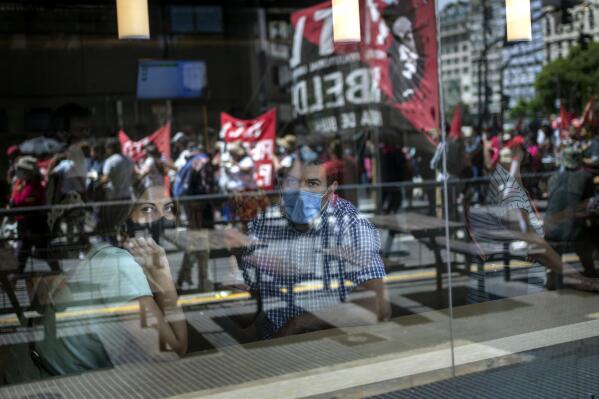 A couple watches a march organized by leftist groups to protest against the government's decision to reach an agreement with the International Monetary Fund (IMF) in Buenos Aires, Argentina, Thursday, Jan. 27, 2022. Argentina has spent three years trying to renegotiate repayment terms on a $45 billion credit the IMF granted in 2018 and considers it vital to stabilizing an economy whose lengthy crisis has been hit as well by the pandemic. (AP Photo/Rodrigo Abd)