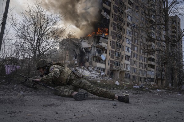A Ukrainian police officer takes cover in front of a burning building that was hit in a Russian airstrike in Avdiivka, Ukraine, March 17, 2023. (AP Photo/Evgeniy Maloletka)