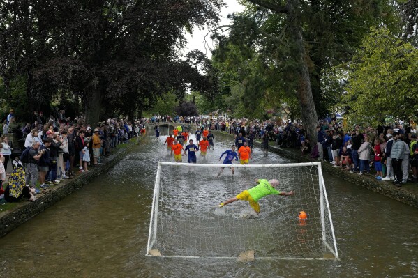 Players from Bourton Rovers compete during the annual traditional River Windrush soccer match, which has been taking place for over 100 years, in the Cotswolds village of Bourton-on-the-Water, England, Monday, Aug. 28, 2023. The event sees two teams of six from Bourton Rovers Football Club play a 30 minute soccer match in the usually calm river water. Goalposts are set up in the river and players attempt to score as many goals as possible, whilst getting all spectators as wet as possible in the process. (AP Photo/Frank Augstein)