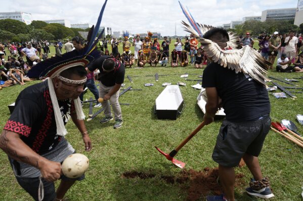 Indigenous people dig a hole for an empty coffin, symbolizing the death of lawmakers who they say are against their rights and territorial protection, during a march at the annual Free Earth camp in Brasilia, Brazil, Tuesday, April 8, 2025. (AP Photo/Eraldo Peres)