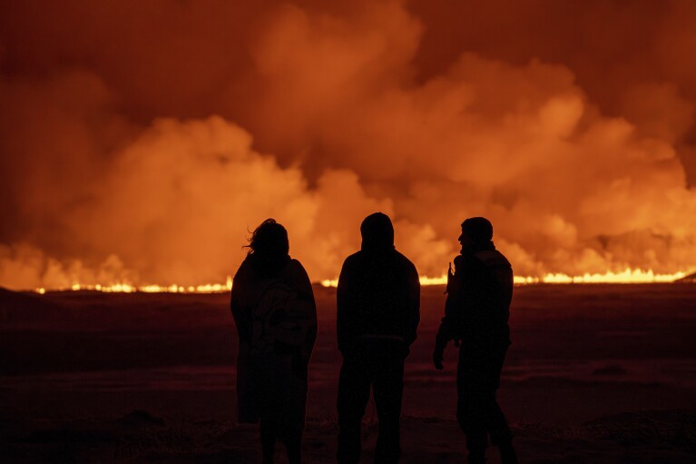 Menschen beobachten, wie der Nachthimmel aufgrund eines Vulkanausbruchs in Grindavik auf der isländischen Halbinsel Reykjanes am Montag, 18. Dezember 2023, aufleuchtet. (AP Photo/Marco DeMarco)