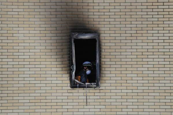 A firefighter is seen through the window of the Kyoto Animation Studio building consumed in an arson attack, Friday, July 19, 2019, in Kyoto, Japan. A man screaming "You die!" burst into the animat...