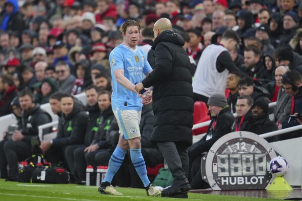 Manchester City's Kevin De Bruyne, left, shakes hands with his coach Pep Guardio after leaving the pitch during the English Premier League soccer match between Liverpool and Manchester City, at Anfield stadium in Liverpool, England, Sunday, March 10, 2024. (AP Photo/Jon Super)