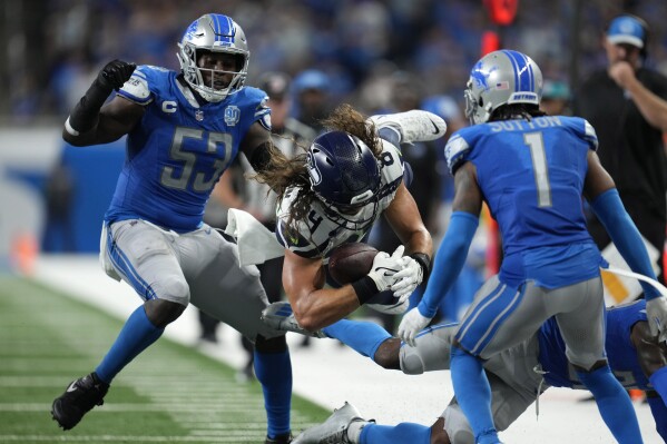 Seattle Seahawks tight end Colby Parkinson (84) dives for extra yardage between Detroit Lions defensive end Charles Harris (53) and cornerback Cameron Sutton (1) during overtime in an NFL football game, Sunday, Sept. 17, 2023, in Detroit. The Seahawks won 37-31. (AP Photo/Paul Sancya)