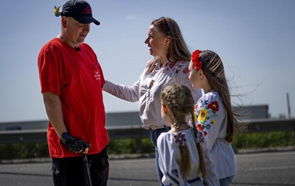 Serhii Khrapko, a Ukrainian war veteran, left, speaks to a woman and her daughters on the highway in the middle of a 120-kilometer (75-mile) walk towards Zhytomyr to meet his friend Oleksandr Shvetsov, to raise money for medical equipment in honor of their comrades wounded in Russia's war against their homeland in Motyzhyn, Ukraine, on Thursday, May 18, 2023. They raised 3.1 million hryvnias ($84,000), short just the 500,000 hryvnias ($14,000) needed to purchase a new gastroscope for Ukraine's National Military Medical Clinical Center. (AP Photo/Roman Hrytsyna)