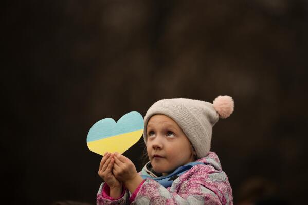 A little girl holds a heart shaped cutout in the colours of the Ukrainian flag, during a protest against Russia's war on Ukraine, marking the first anniversary of Russia's full-scale invasion of Ukraine, in Bucharest, Romania, Friday, Feb. 24, 2023. (AP Photo/Andreea Alexandru)