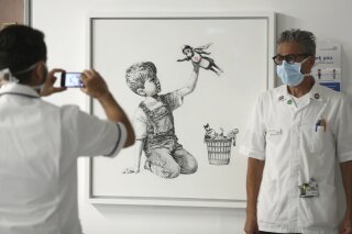A member of staff has their photograph taken in front of the new artwork painted by Banksy during lockdown, entitled 'Game Changer', which has gone on display to staff and patients on Level C of Southampton General Hospital in Southampton, England, Thursday, May 7, 2020. (Andrew Matthews/PA via AP)
