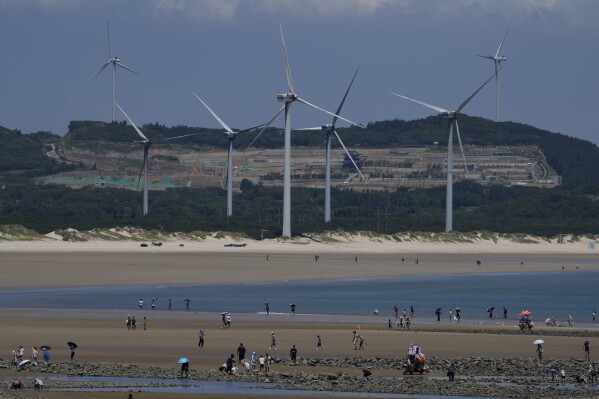 FILE - Beachgoers walk near wind turbines along the coast of Pingtan in Southern China's Fujian province, on Aug. 6, 2022. According to a new report published Tuesday, April 16, 2024, last year, marked the best year for new wind projects. (AP Photo/Ng Han Guan, File)