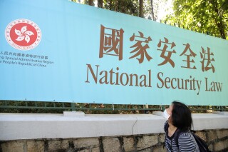 FILE - A woman walks past a promotional banner of the national security law for Hong Kong, in Hong Kong, on June 30, 2020. A group that promotes Cantonese shut down on Monday, Aug. 28, 2023 after Hong Kong authorities accused an essay submitted to a competition it held three years ago of violating the national security law, in the latest example of the city's erosion of freedom of expression. (AP Photo/Kin Cheung, File)