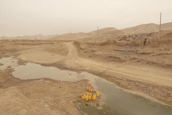 Oil canisters used to carry water stand in the middle of the riverbed of dried-out river, in Sang-e-Atash, Afghanistan, Monday, Dec. 13, 2021. Severe drought has dramatically worsened the already desperate situation in Afghanistan forcing thousands of people to flee their homes and live in extreme poverty. Experts predict climate change is making such events even more severe and frequent. (AP Photo/Mstyslav Chernov)