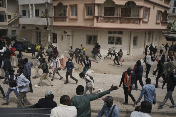 People run from tear gas thrown by riot police after the opposition leader's Ousmane Sonko left the tribunal in Dakar, Senegal, Thursday, Feb. 16, 2023. Police in Senegal smashed out the windows of the Sonko's car and forced him from the vehicle after he appeared in court. (AP Photo/Leo Correa)