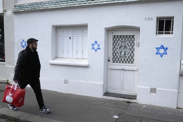 A man walks by Stars of David tagged on a wall Tuesday, Oct. 31, 2023 in Paris. Paris police chief Laurent Nunez described the graffiti as anti-Semitic and said police are investigating. (AP Photo/Michel Euler, Pool)