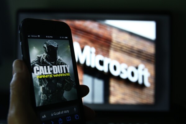 File - An image from Activision's Call of Duty is shown on a smartphone near a photograph of the Microsoft logo in this photo taken in New York, Thursday, June 15, 2023. A judge handed Microsoft a big victory on Tuesday, declining to stop its $69 billion takeover of video game maker Activision Blizzard. (AP Photo/Peter Morgan, File)