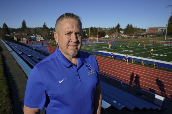 FILE - Joe Kennedy, a former assistant football coach at Bremerton High School in Bremerton, Wash., poses for a photo March 9, 2022, at the school's football field. Years after Kennedy left the Bremerton High School football team over objections to his post-game praying on the field, he has returned to the gridiron thanks to a Supreme Court decision, and his first game back is Friday, Sept. 1, 2023. (AP Photo/Ted S. Warren, File)