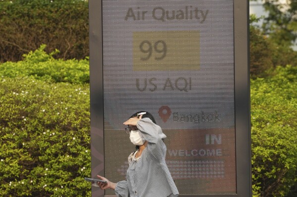 A pedestrian wears a face mask in front of a sign displaying an Air Quality Index in Bangkok, Thailand, Feb. 6, 2025. (AP Photo/Sakchai Lalit, File)