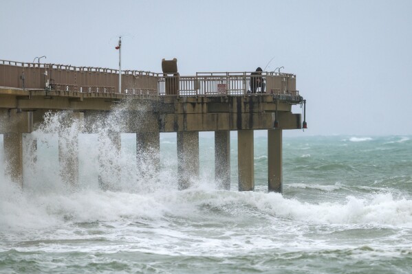 A person fishes on the Newport Fishing Pier in Sunny Isles Beach, Fla., on Thursday, Dec. 14, 2023, as the gusty winds, heavy rain, flooded streets and other hazards are expected continue over the weekend in Miami, Fort Lauderdale and Palm Beach. (David Santiago/Miami Herald via AP)