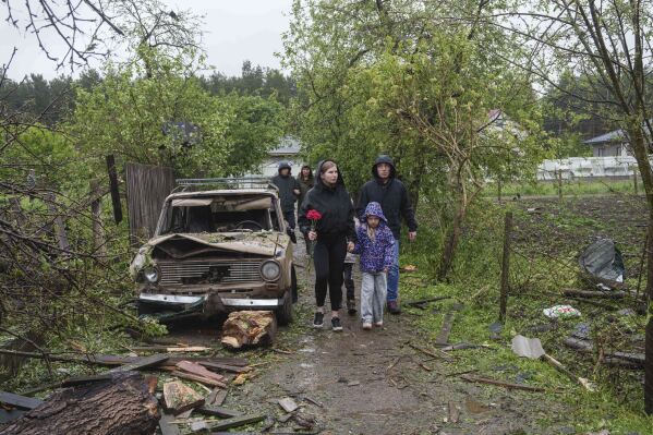 People carry flowers to the rubble of a destroyed house where three children were killed by a Russian strike in Korostyshiv, Zhytomyr region, Ukraine, Sunday, May 25, 2025. (AP Photo/Evgeniy Maloletka)
