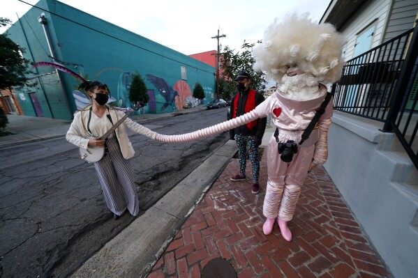 Hannah Standiford holds hands with her friend Varia Degtiairenko, right, in a socially distanced fashion in the Bywater section of New Orleans on Mardi Gras Day, Feb. 16, 2021. (AP Photo/Gerald Herbert, file)