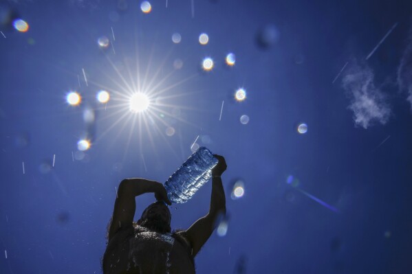 FILE - A man pours cold water onto his head to cool off on a sweltering hot day in the Mediterranean Sea in Beirut, Lebanon, Sunday, July 16, 2023. In the past 30 days, nearly 5,000 heat and rainfall records have been broken or tied in the United States and more than 10,000 records set globally, according to the National Oceanic and Atmospheric Administration. Since 2000, the U.S. is setting about twice as many heat records as cold. (AP Photo/Hassan Ammar, File)